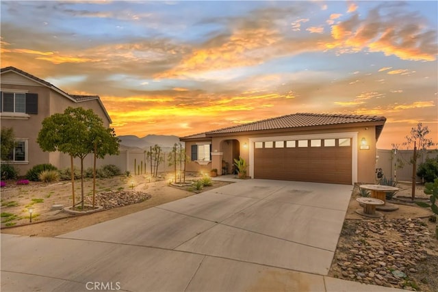 view of front of house featuring stucco siding, a tiled roof, fence, a garage, and driveway