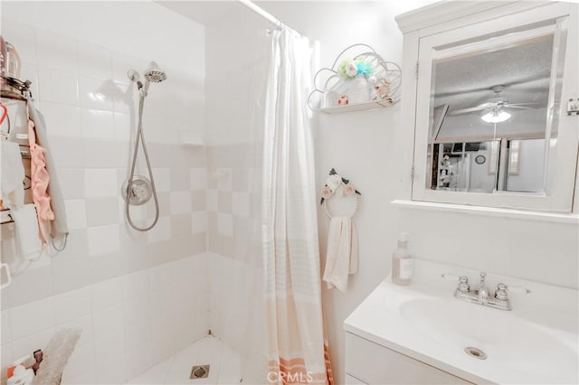full bath featuring a ceiling fan, vanity, and a tile shower
