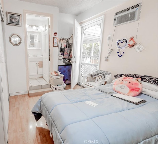 bedroom featuring wood finished floors, ensuite bath, baseboards, access to outside, and a wall unit AC