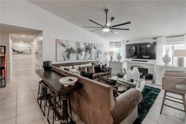 living area featuring vaulted ceiling, a textured ceiling, light tile patterned flooring, ceiling fan, and a brick fireplace
