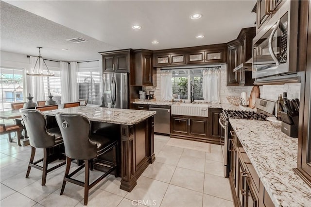 kitchen with dark brown cabinets, visible vents, decorative backsplash, light stone counters, and appliances with stainless steel finishes