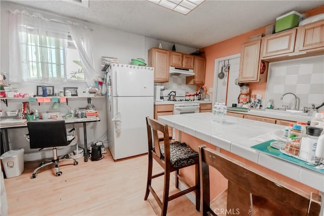 kitchen with tile counters, a sink, white appliances, light brown cabinets, and under cabinet range hood