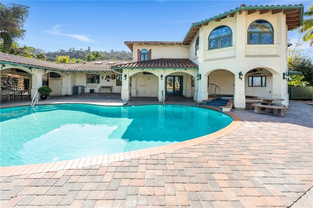 rear view of house with central air condition unit, a tiled roof, and an outdoor pool