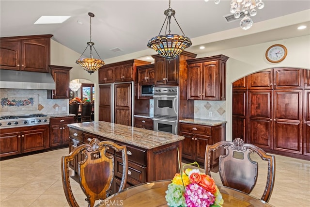 kitchen with under cabinet range hood, light stone counters, appliances with stainless steel finishes, and tasteful backsplash