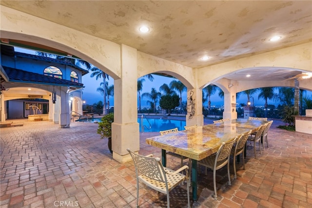 patio at twilight with outdoor dining area and an outdoor pool