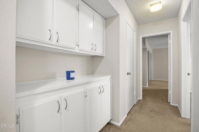 hall featuring baseboards, light carpet, and a textured ceiling
