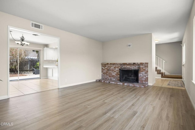 unfurnished living room featuring an inviting chandelier, a brick fireplace, wood finished floors, visible vents, and stairway