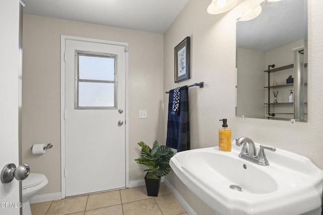 bathroom featuring baseboards, toilet, tile patterned floors, and a sink
