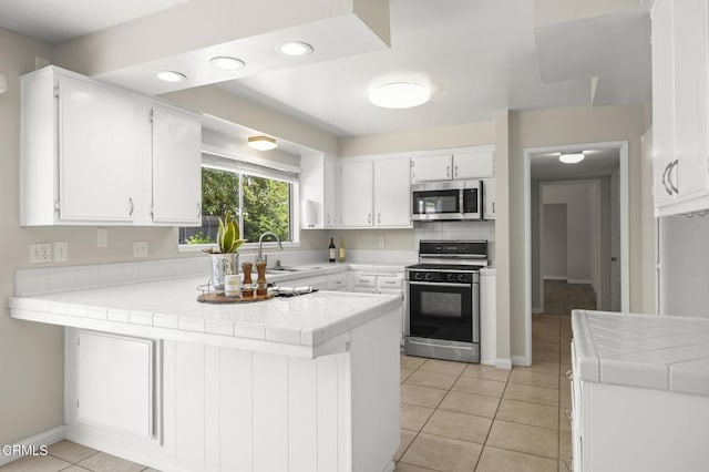 kitchen with a peninsula, tile countertops, stainless steel microwave, range with gas cooktop, and a sink