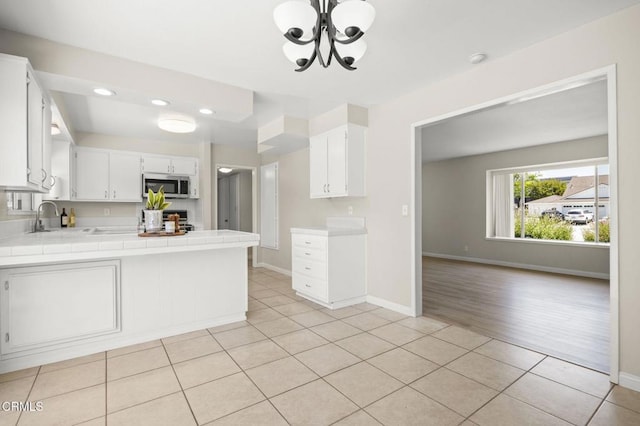 kitchen with light tile patterned flooring, tile counters, stainless steel microwave, a sink, and a notable chandelier