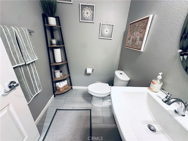 half bath with toilet, a sink, and baseboards