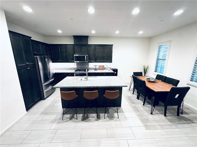 kitchen with recessed lighting, a sink, light stone countertops, a center island with sink, and appliances with stainless steel finishes
