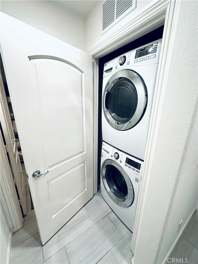 clothes washing area featuring stacked washer and dryer, visible vents, and laundry area