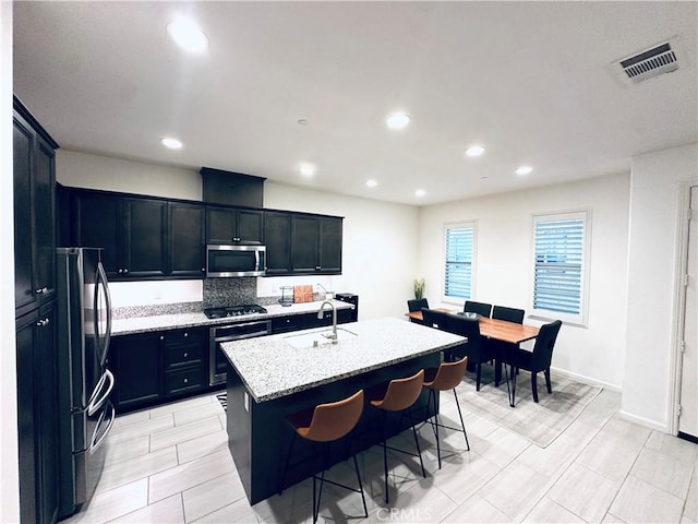 kitchen featuring visible vents, gas cooktop, stainless steel microwave, freestanding refrigerator, and a sink