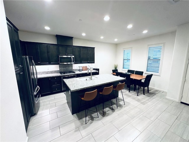 kitchen featuring light stone counters, a sink, a breakfast bar area, stainless steel appliances, and a center island with sink