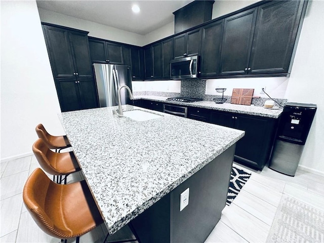 kitchen with a sink, a breakfast bar, baseboards, appliances with stainless steel finishes, and light stone countertops