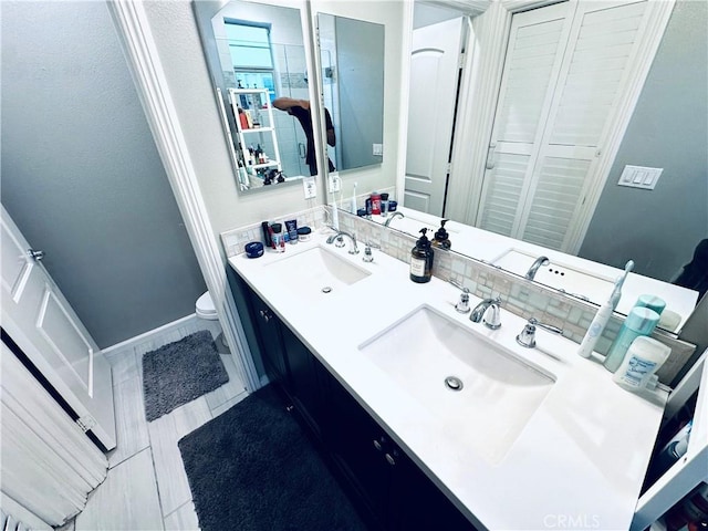 full bath with double vanity, toilet, baseboards, and a sink