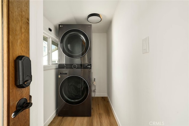clothes washing area with wood finished floors, stacked washer and dryer, baseboards, and laundry area