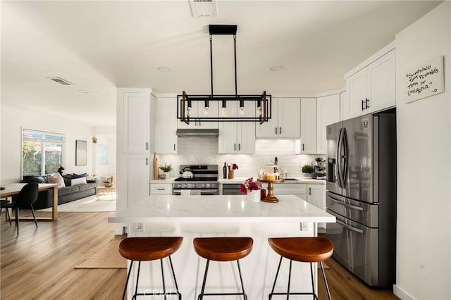 kitchen featuring dark wood finished floors, stainless steel appliances, backsplash, a breakfast bar, and visible vents