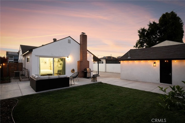 rear view of property featuring a yard, a patio area, a chimney, and stucco siding
