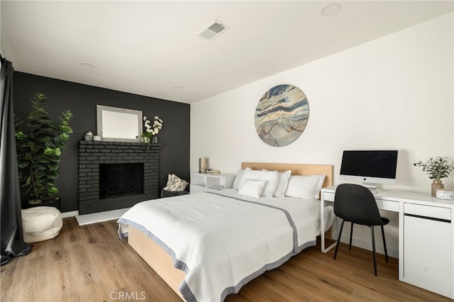 bedroom featuring baseboards, light wood finished floors, visible vents, and a fireplace