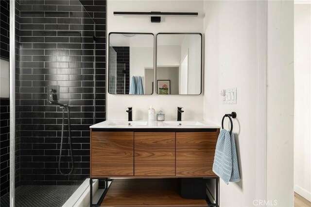 full bathroom with wood finished floors, a sink, double vanity, and tiled shower