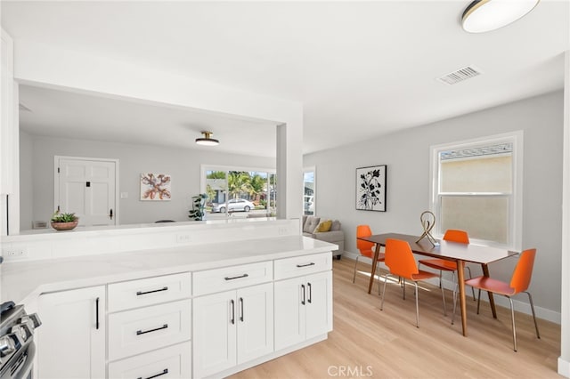 kitchen with light countertops, visible vents, light wood-type flooring, gas range, and white cabinetry