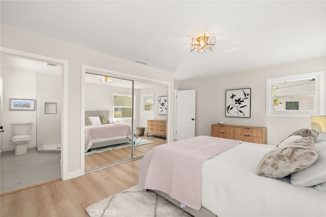 bedroom featuring ensuite bathroom, multiple windows, visible vents, and light wood-type flooring