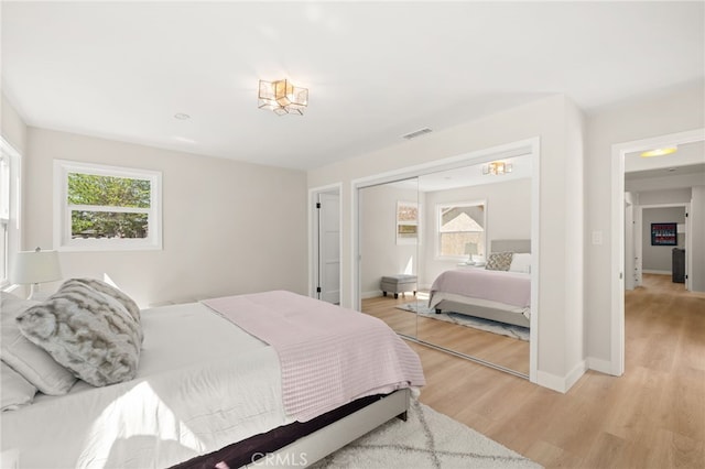 bedroom with baseboards, light wood-style floors, visible vents, and a closet