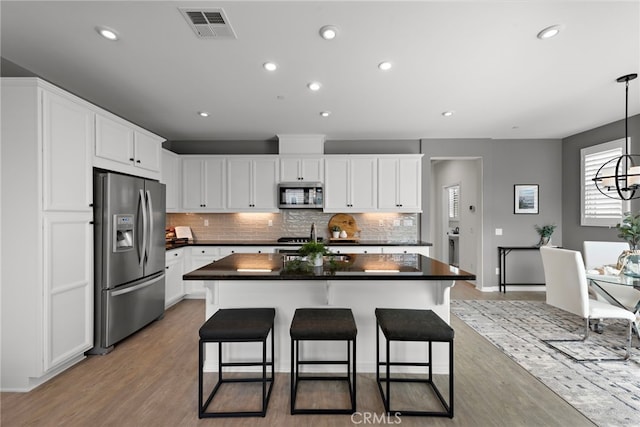 kitchen featuring stainless steel appliances, dark countertops, visible vents, a kitchen island, and tasteful backsplash