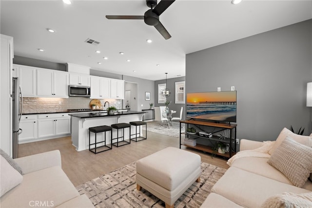 living room featuring recessed lighting, light wood-type flooring, visible vents, and ceiling fan with notable chandelier