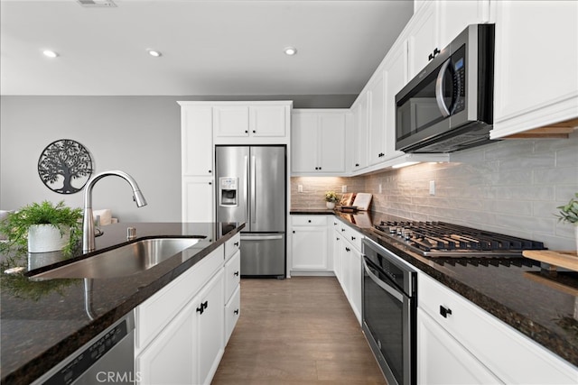 kitchen featuring white cabinets, appliances with stainless steel finishes, dark stone counters, and a sink