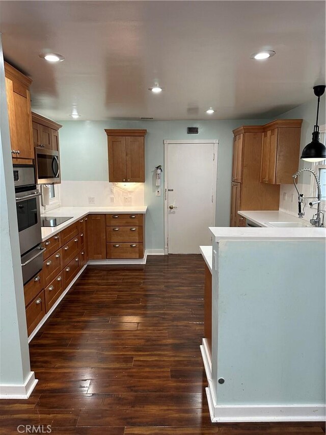 kitchen with brown cabinetry, stainless steel appliances, dark wood-style flooring, and a sink