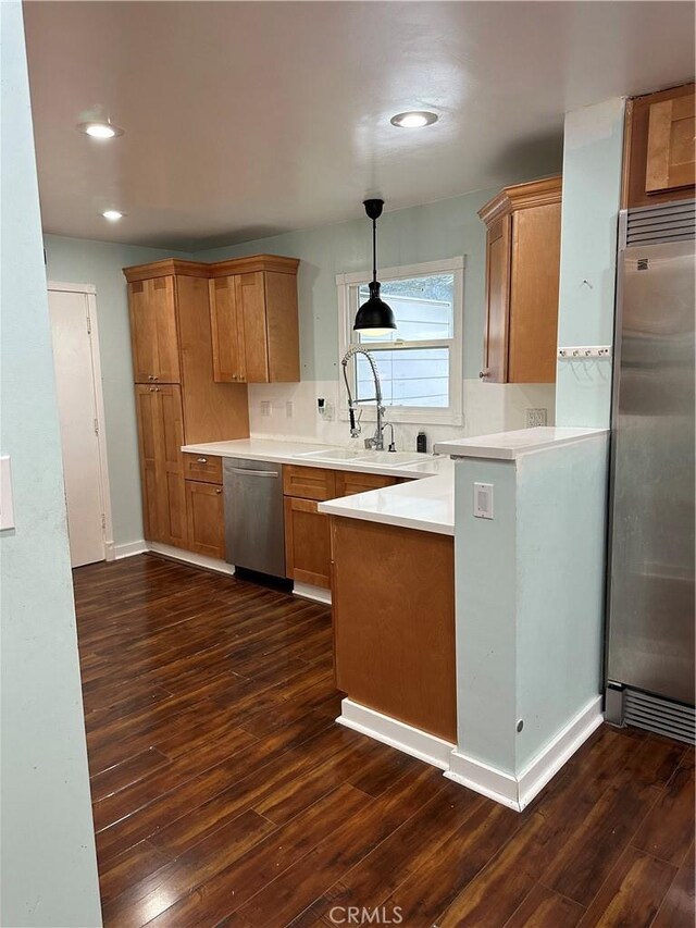 kitchen with dark wood-style floors, a sink, backsplash, a peninsula, and appliances with stainless steel finishes
