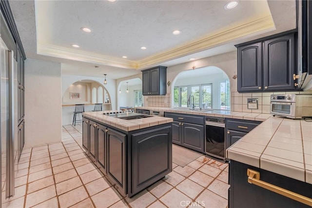 kitchen featuring tile counters, arched walkways, a sink, and a tray ceiling