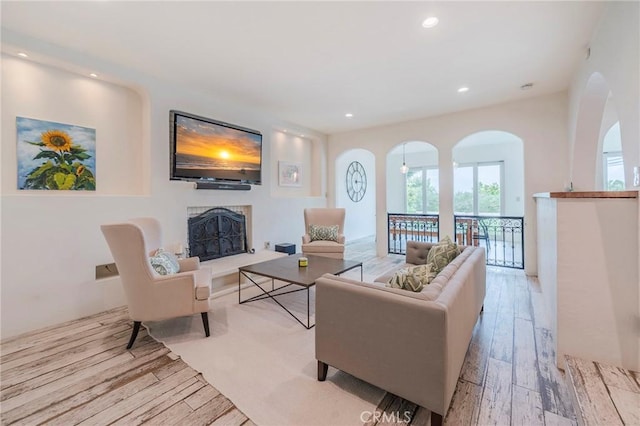 living room featuring recessed lighting, arched walkways, light wood finished floors, and a fireplace with raised hearth