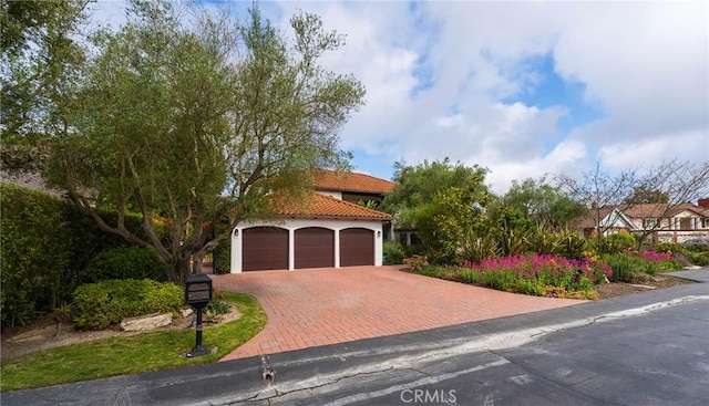 mediterranean / spanish house with an attached garage, stucco siding, a tile roof, and decorative driveway
