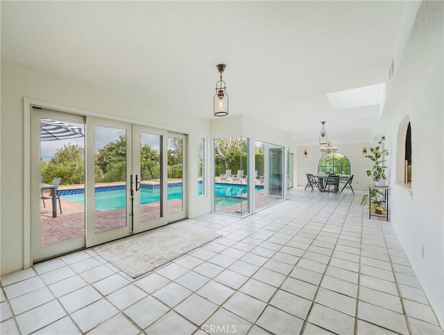 sunroom / solarium featuring french doors, a skylight, and an inviting chandelier