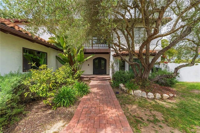 property entrance featuring french doors, a balcony, and stucco siding