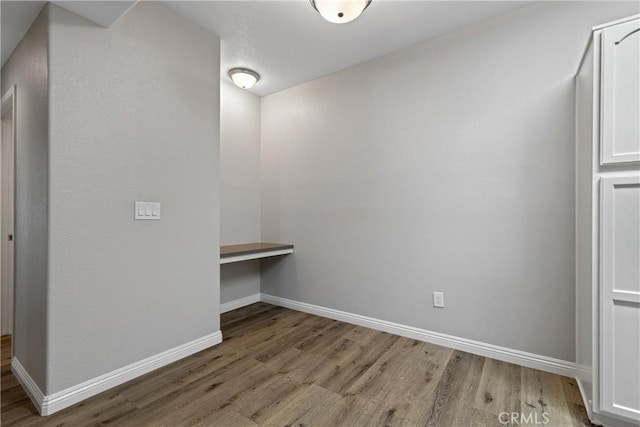 unfurnished room featuring baseboards, built in desk, and wood finished floors
