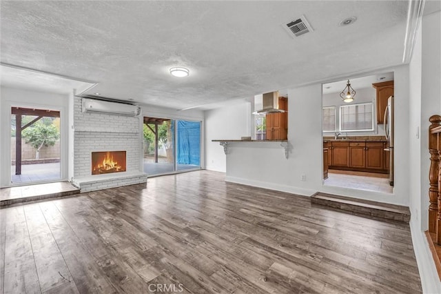 unfurnished living room featuring a sink, a healthy amount of sunlight, visible vents, wood finished floors, and a wall mounted AC
