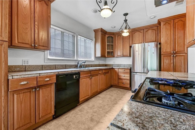 kitchen featuring dishwasher, brown cabinetry, a sink, and freestanding refrigerator