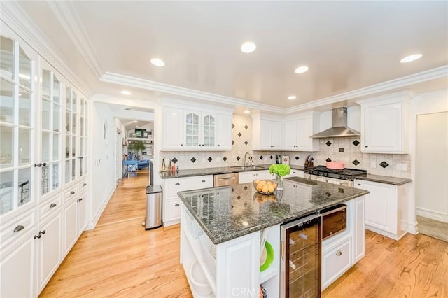 kitchen featuring wall chimney range hood, open shelves, white cabinetry, beverage cooler, and light wood-style flooring