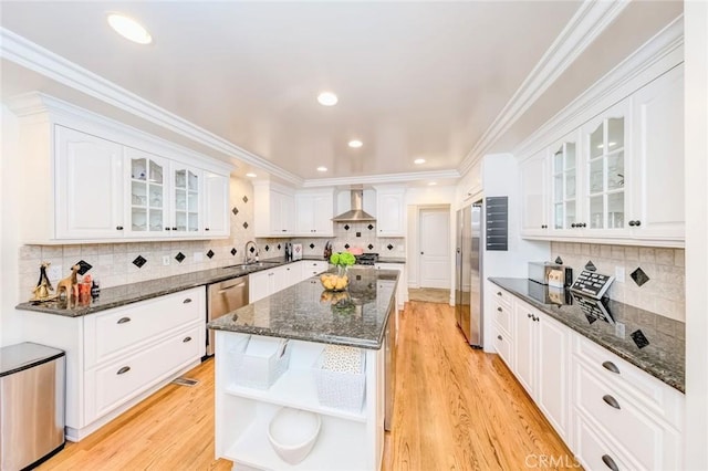 kitchen featuring open shelves, a sink, light wood finished floors, stainless steel appliances, and wall chimney exhaust hood