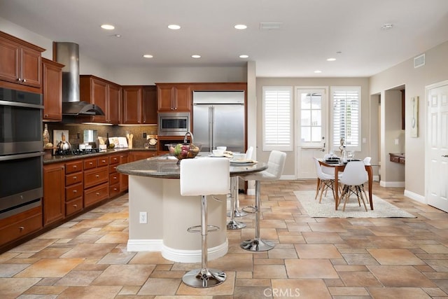 4505 Cresta Babia, San Clemente, CA 92673 - kitchen with built in appliances, wall chimney range hood, brown cabinetry, a breakfast bar area, and backsplash