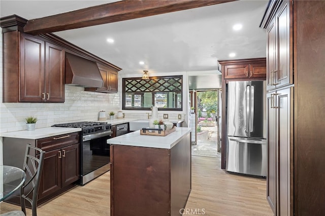 kitchen with light wood finished floors, backsplash, light countertops, wall chimney exhaust hood, and appliances with stainless steel finishes