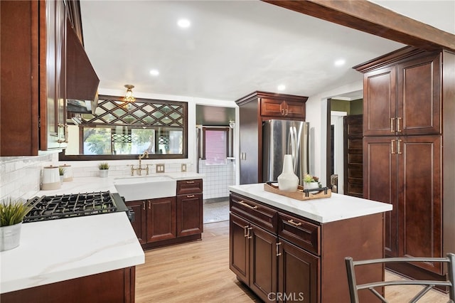 kitchen with a sink, light wood finished floors, gas range oven, backsplash, and freestanding refrigerator