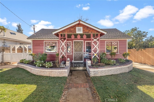 view of front of property featuring a shingled roof, a front lawn, and fence