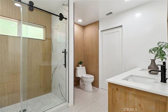 full bathroom featuring wood finished floors, a marble finish shower, a sink, toilet, and visible vents