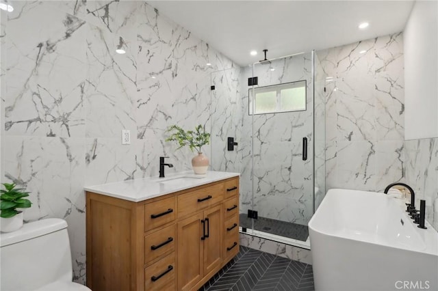 full bathroom featuring a freestanding bath, toilet, vanity, a marble finish shower, and tile walls